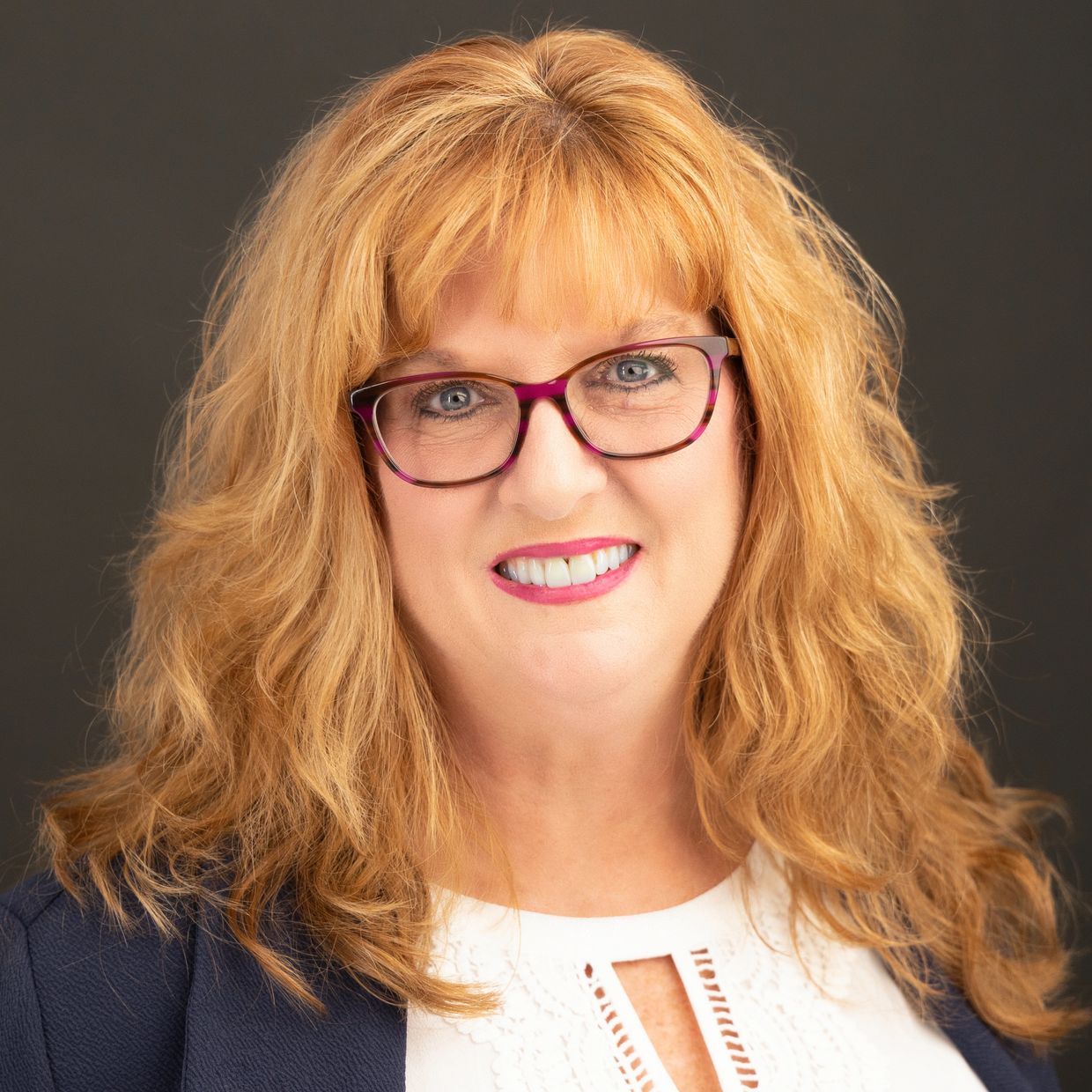 Smiling woman with red hair and glasses.