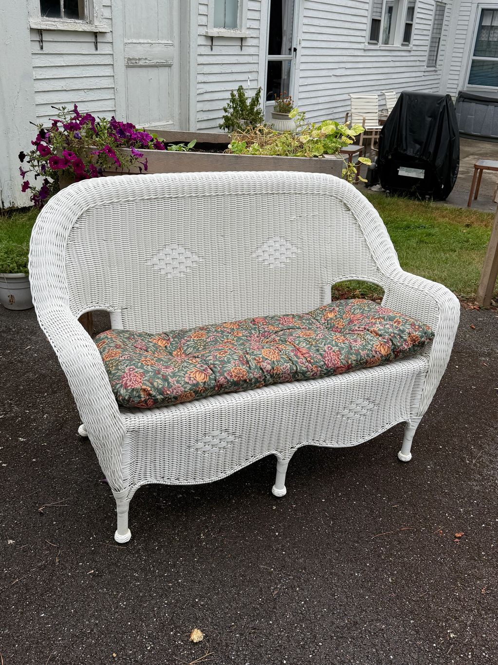 White wicker bench with floral cushion outdoors.