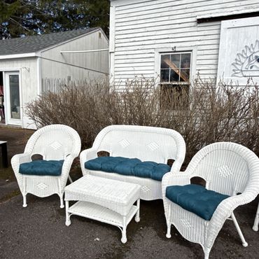 White wicker outdoor furniture with blue cushions arranged near a white building.