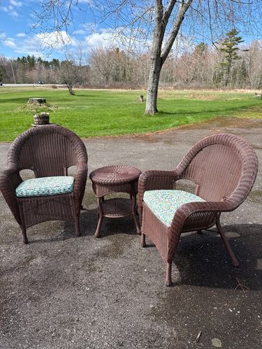 Two wicker chairs with cushions and a small wicker table outdoors on a sunny day.