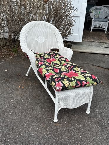 White wicker chaise lounge with floral cushion on outdoor pavement.