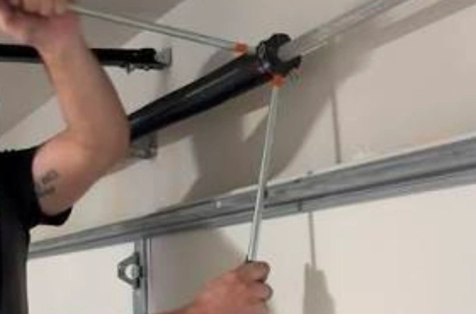 Person tightening a garage door spring with tools.