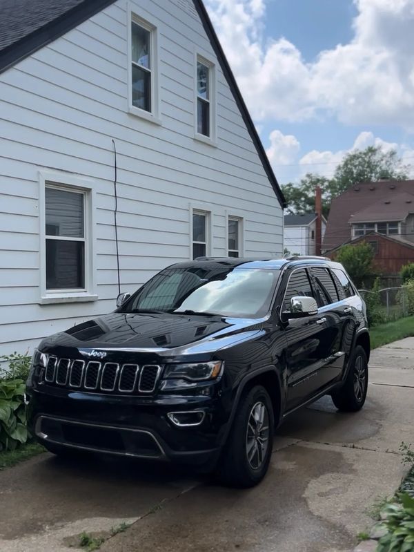 A black Jeep SUV parked on a driveway beside a white house under a blue sky.