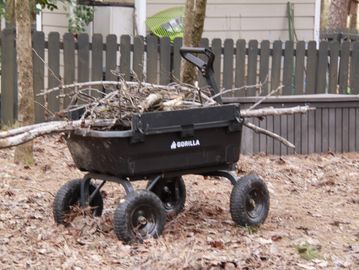A black Gorilla cart filled with tree branches in a yard.