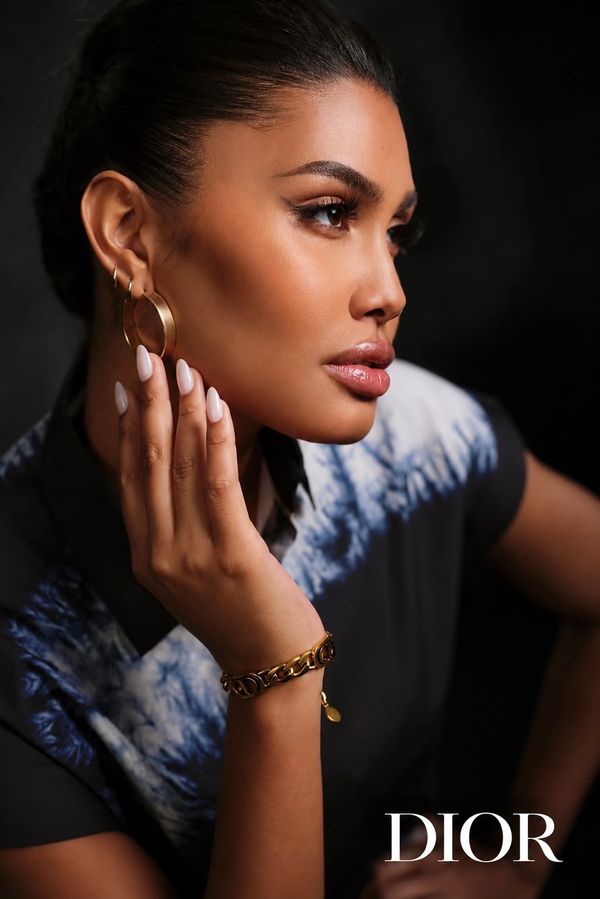 Close-up of a woman wearing gold jewelry and a stylish top, posing elegantly against a dark background.