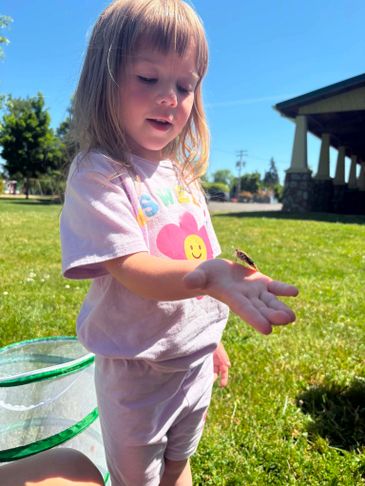 A young girl holding a small frog on her hand outdoors.
