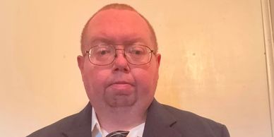 Man in glasses and suit against a beige background.