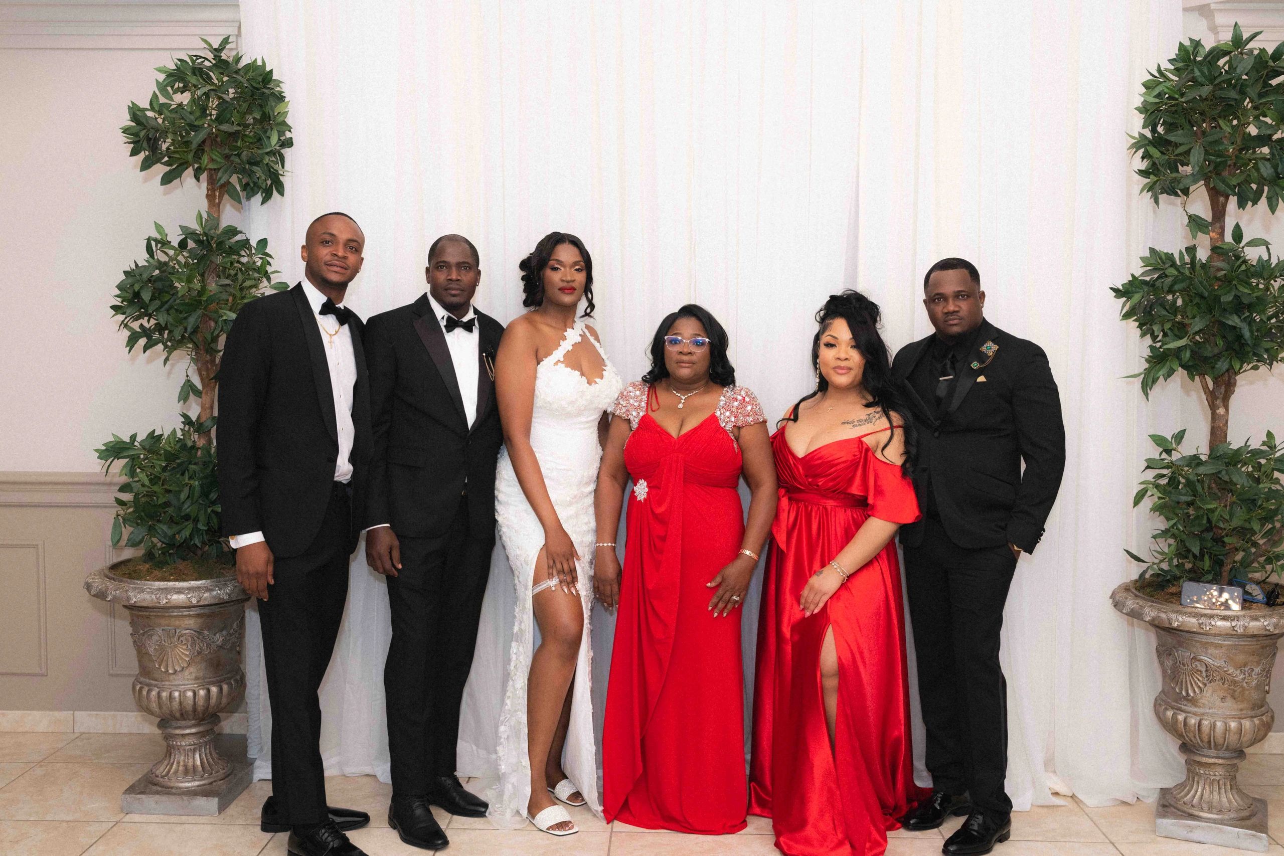 Group of six people dressed formally, three women in red and white dresses, three men in black suits.