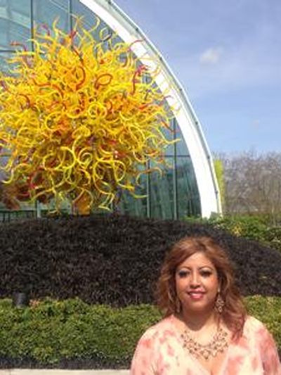 Woman posing outdoors near a colorful glass sculpture.