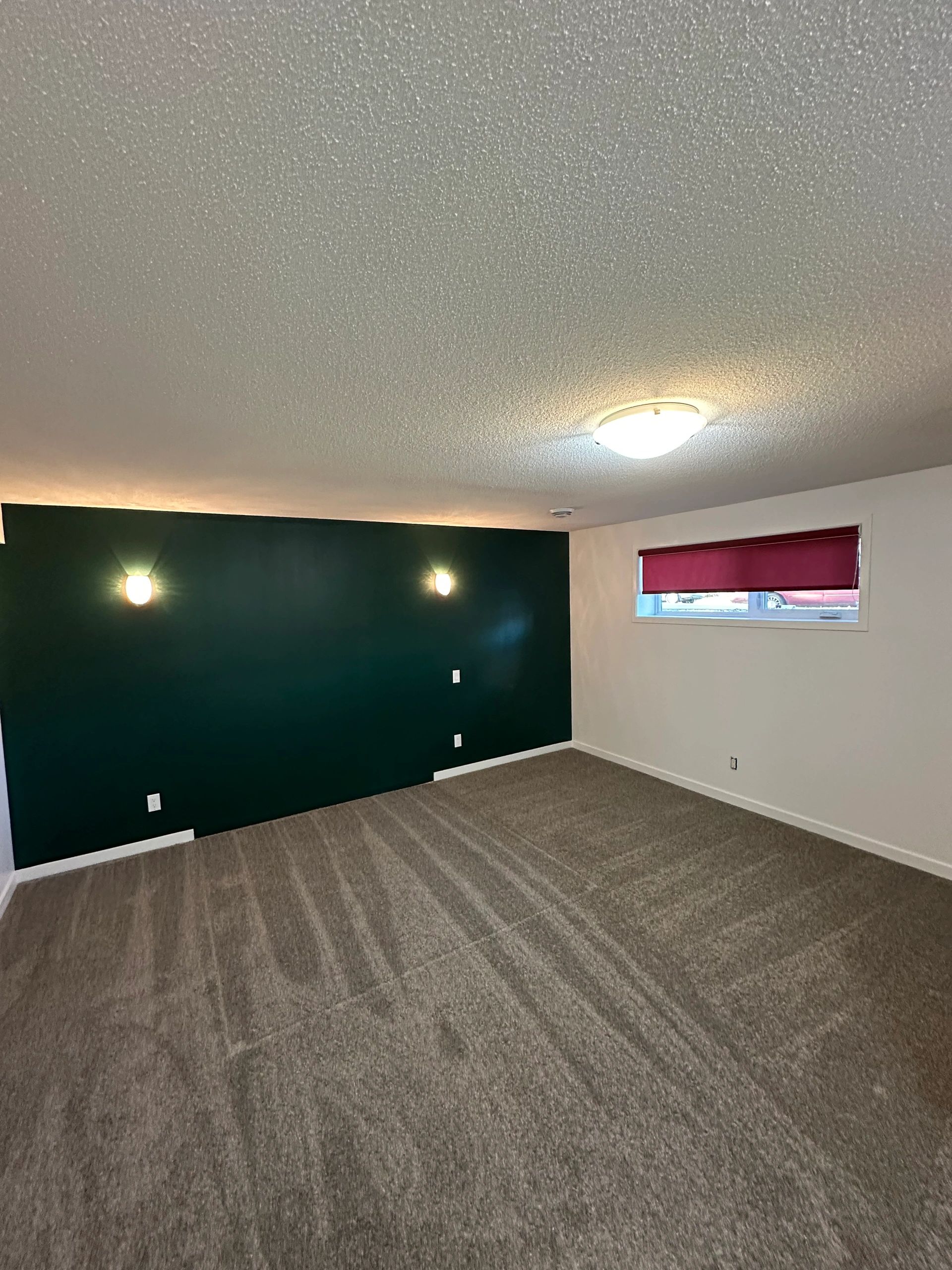 Empty room with dark green accent wall, beige carpet, and red window blind.