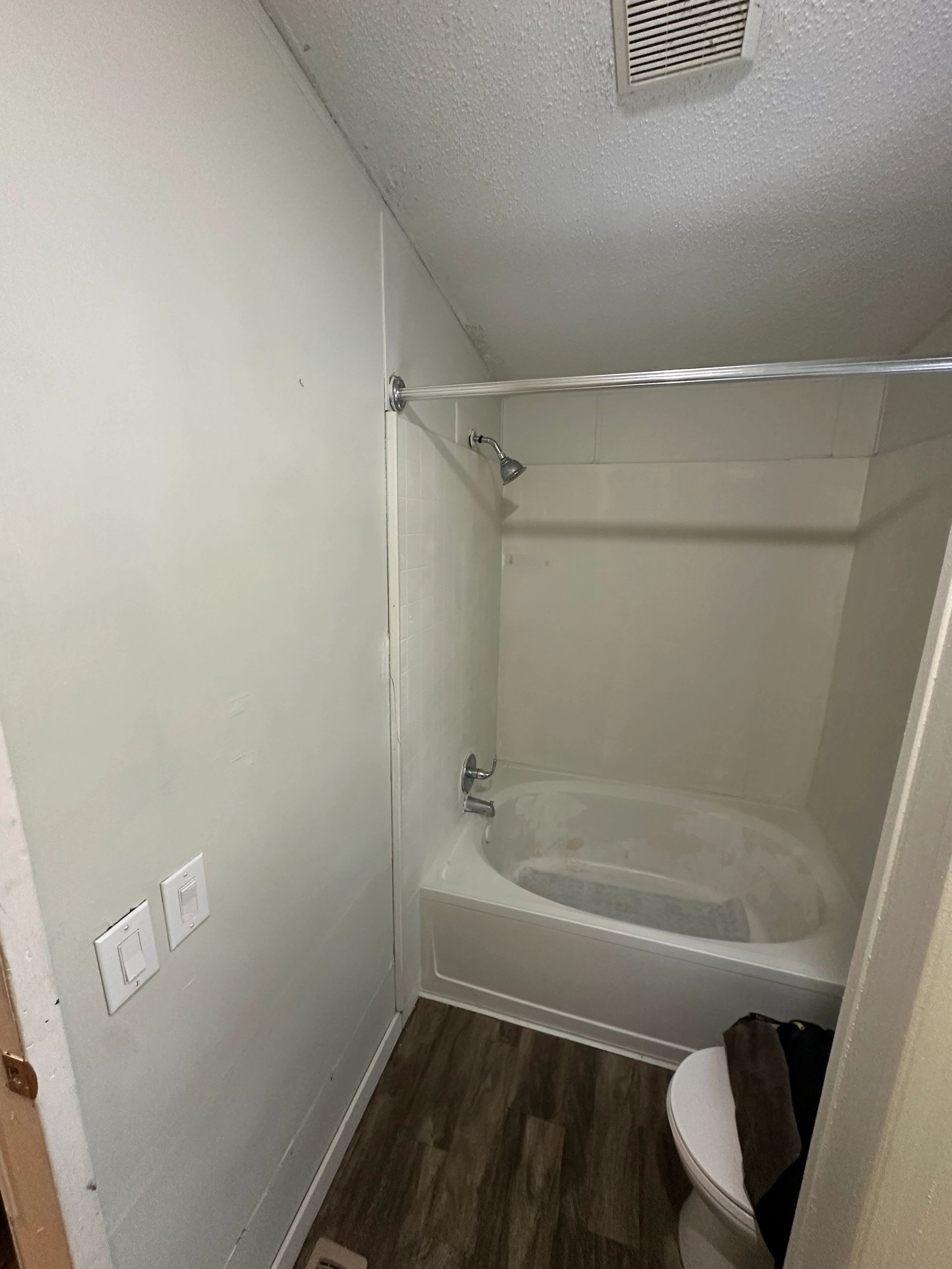 Small bathroom with bathtub, shower, toilet, and wooden floor.