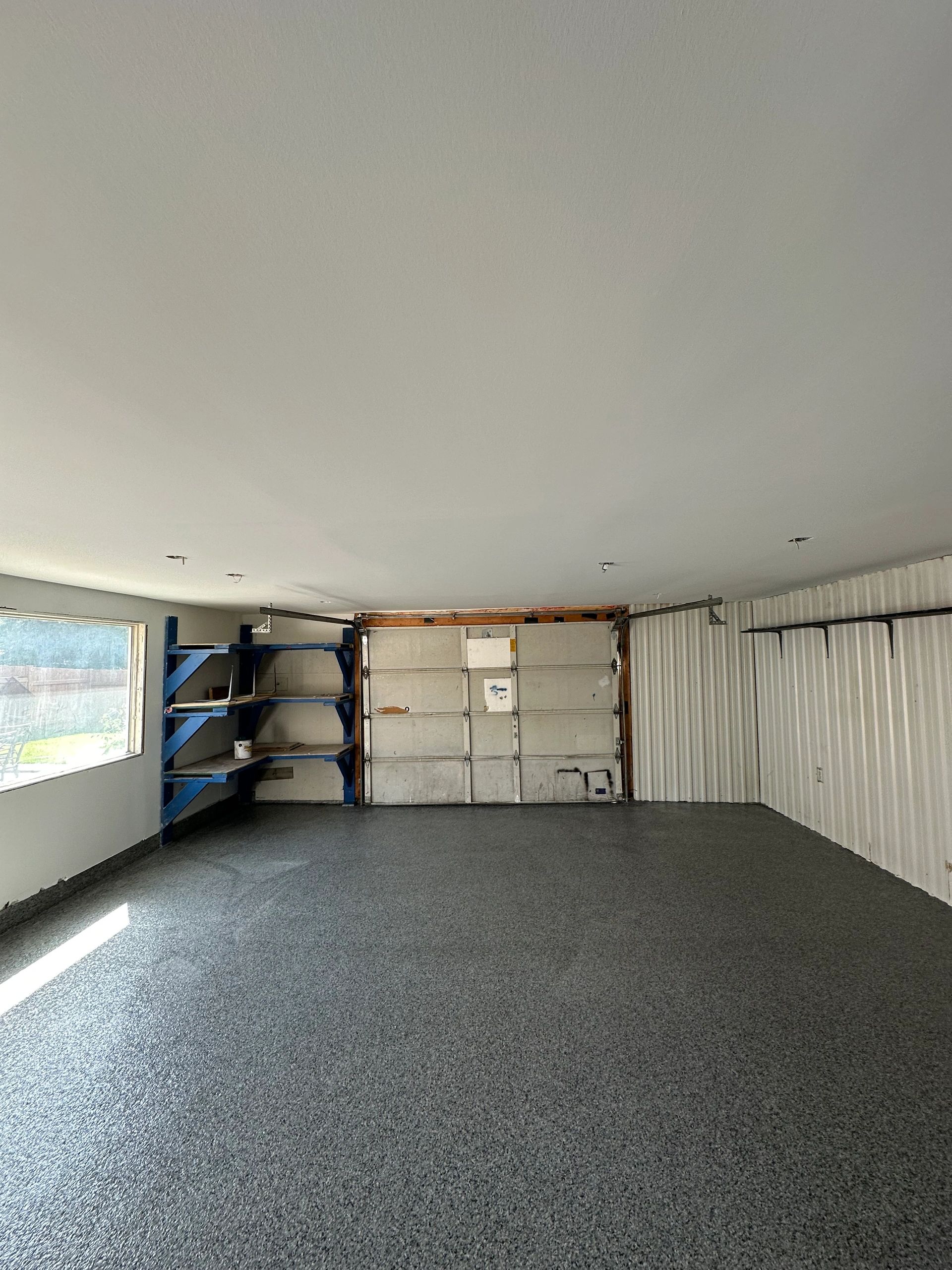Empty garage with blue shelves and a large window letting in natural light.