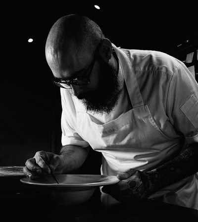 A focused chef meticulously plating a dish in a dimly lit kitchen.
