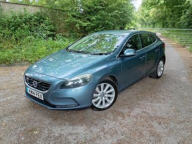Blue Volvo parked on a rural road near a metal gate.