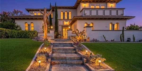 Lit pathway leading to a large, elegant house at dusk.
