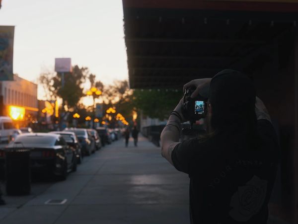 Person taking a photo of a sunset on a city street.