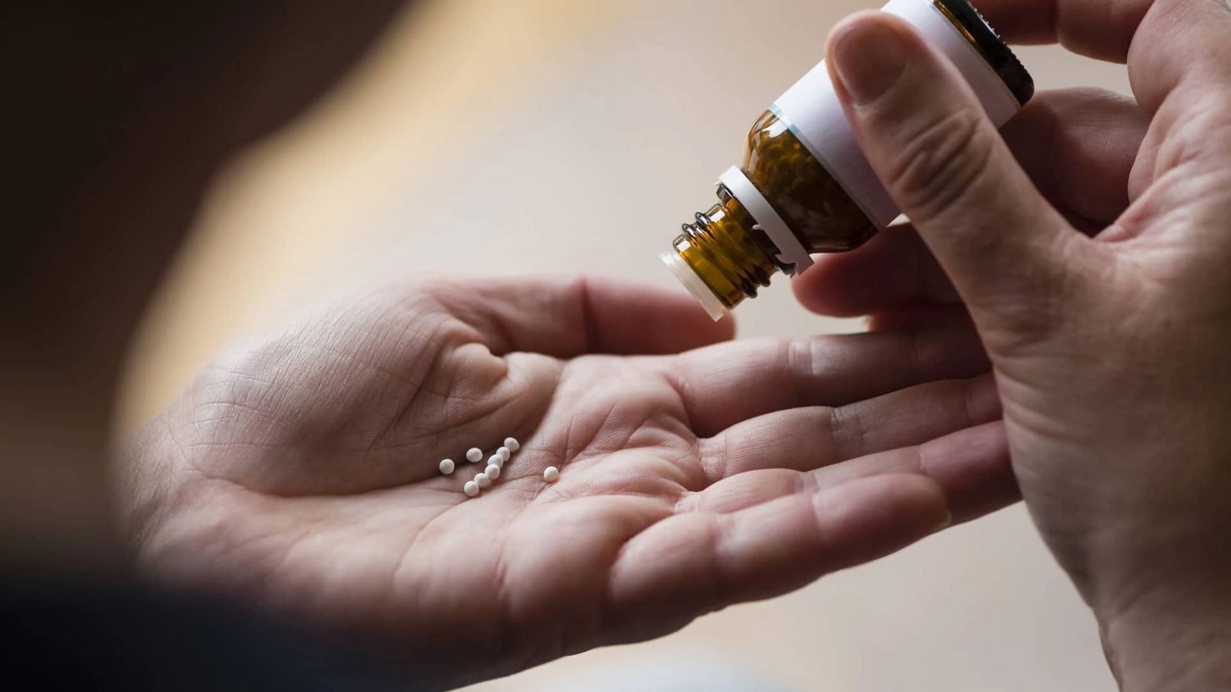 Person pouring small white pills from a brown bottle into their hand.
