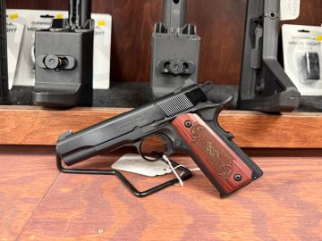 A handgun displayed on a wooden surface with gun accessories in the background.