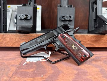 A Browning handgun displayed on a wooden surface with a tag attached.