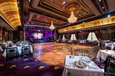 Elegant dining room with stage and chandeliers in a grand venue.