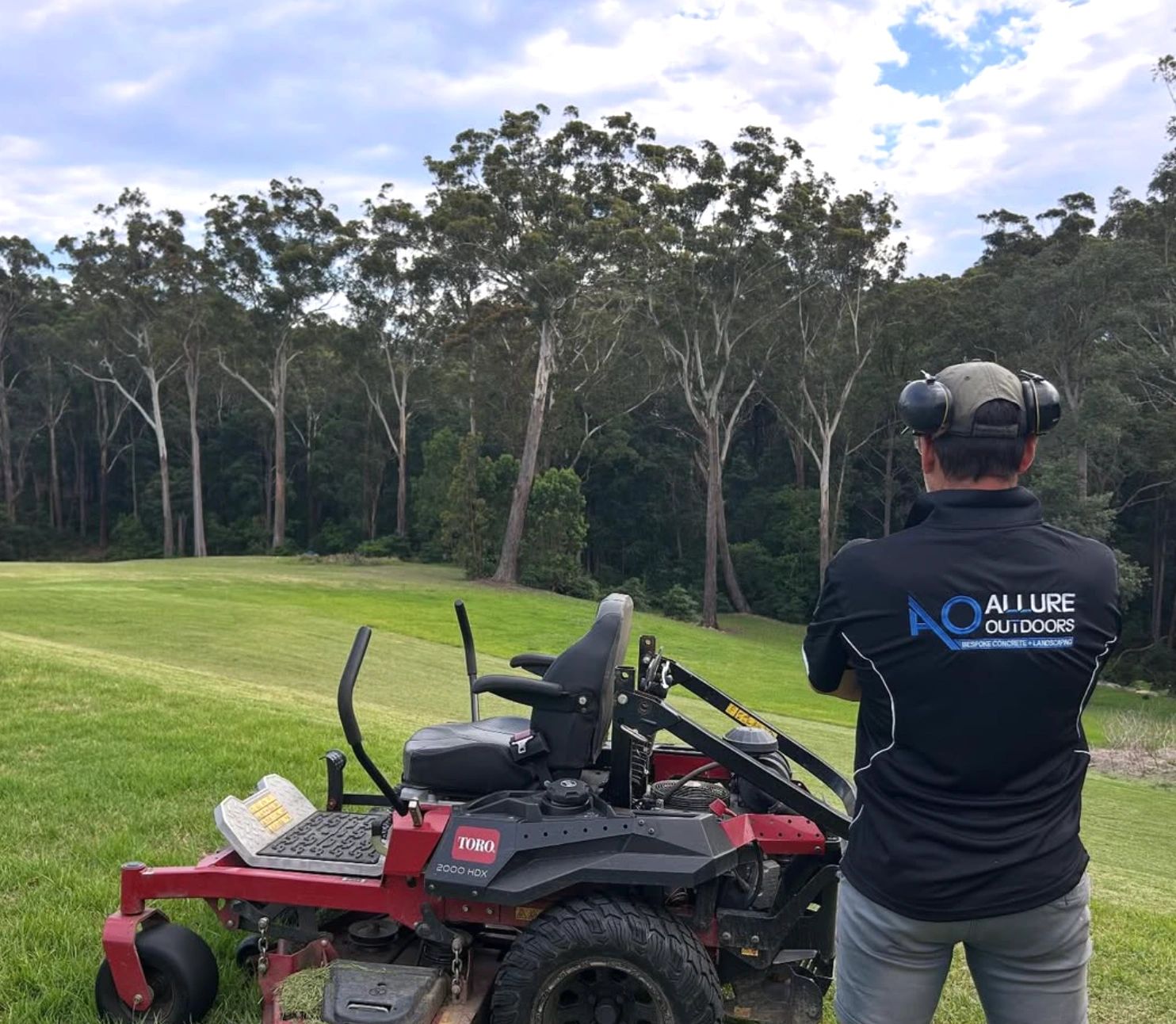 Man standing next to a Toro 2000 HDX lawn mower on a green field.