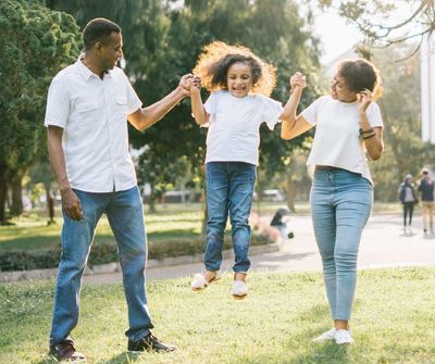 A father, daughter, and mother joyfully playing in a park.