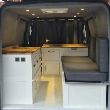 Compact camper van interior with modern kitchen and seating area.