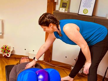 A woman assists another lying down during a physical therapy session.