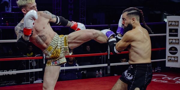 Two male fighters in a boxing ring, one delivering a high kick to the other's head.