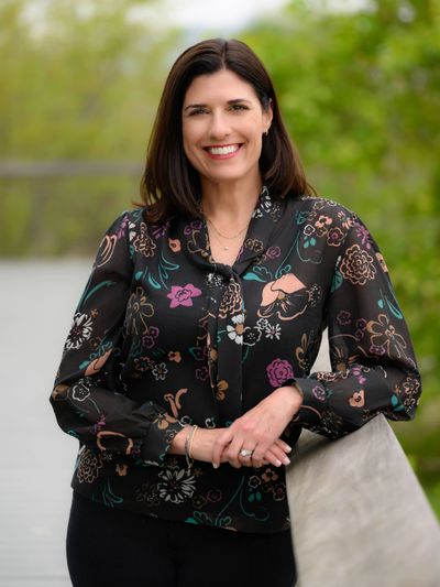 A photo of Karie Reynolds standing outdoors wearing a black shirt with colorful flowers and black pa