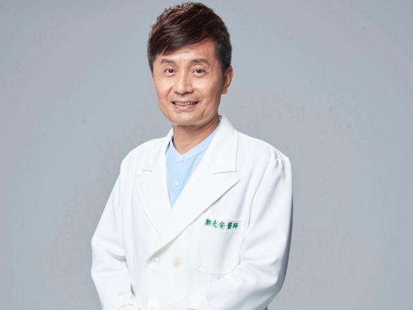 Smiling male doctor in white coat against gray background.