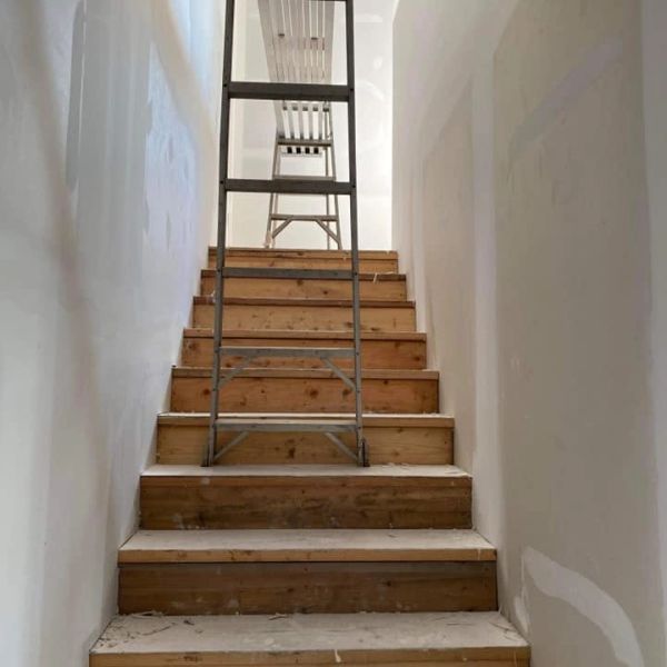 A ladder positioned on wooden stairs with a chair at the top.