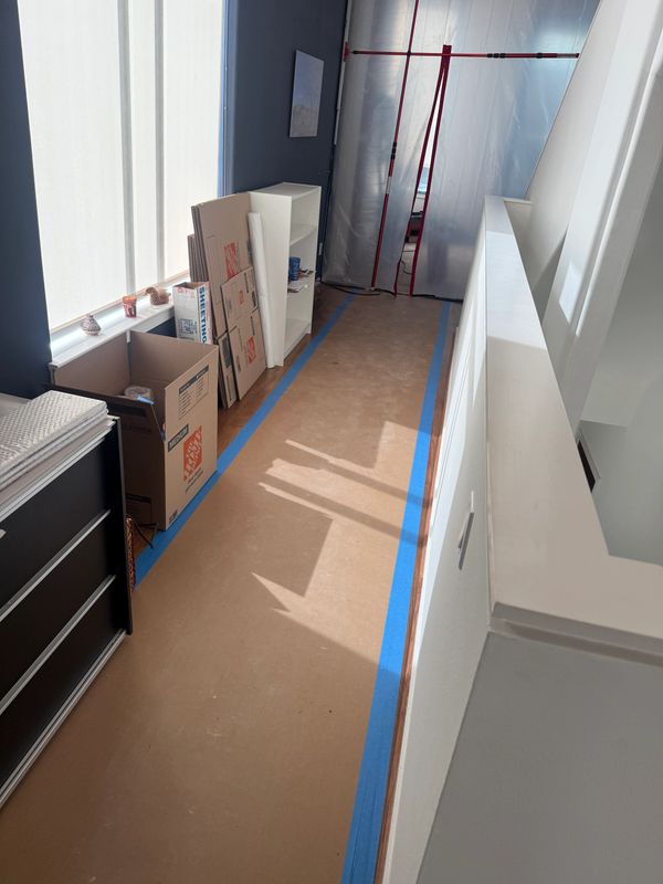 A hallway under renovation with protective floor covering and packing boxes.