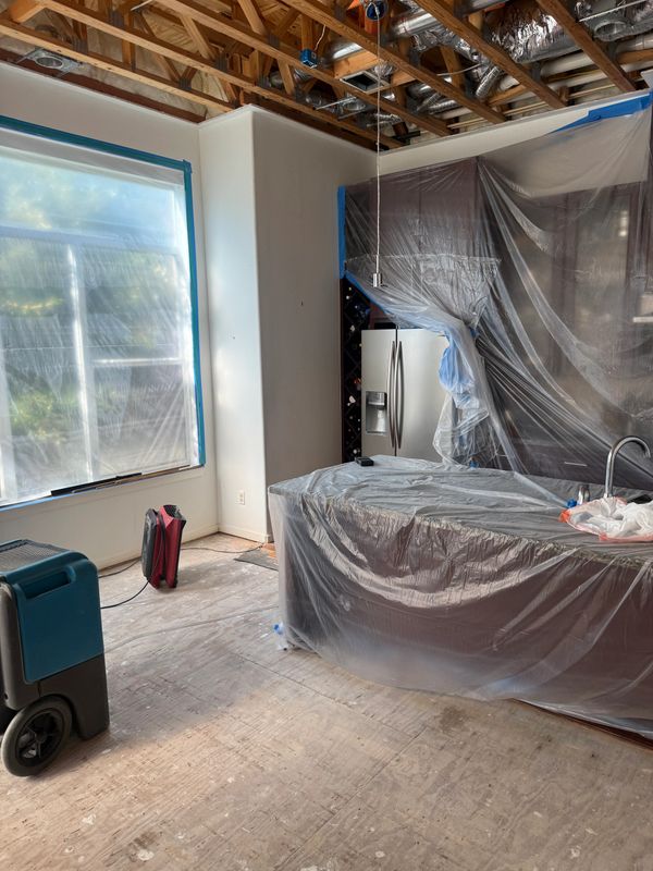 Kitchen under renovation with plastic coverings and exposed ceiling.