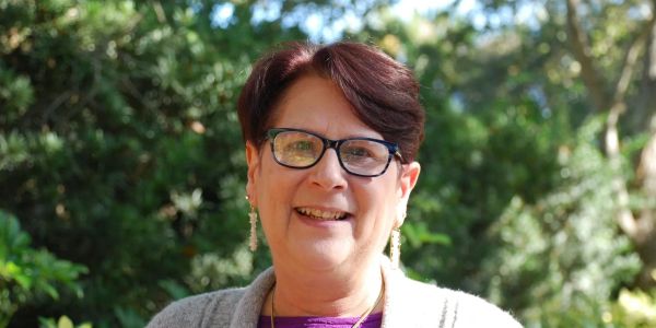 Smiling woman with glasses outdoors in sunlight.