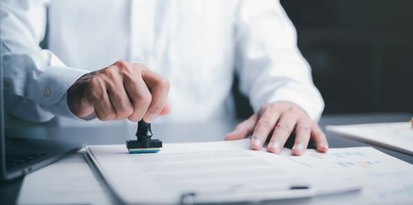 Man in a suit who is stamping paperwork on a desk