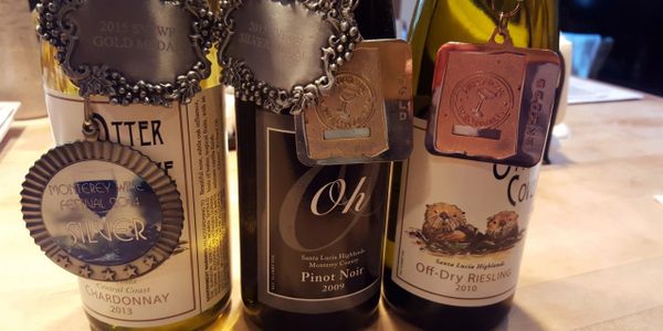 Three wine bottles each adorned with multiple award medals on a wooden surface.