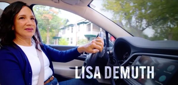 Woman driving a car with the name Lisa Demuth displayed.