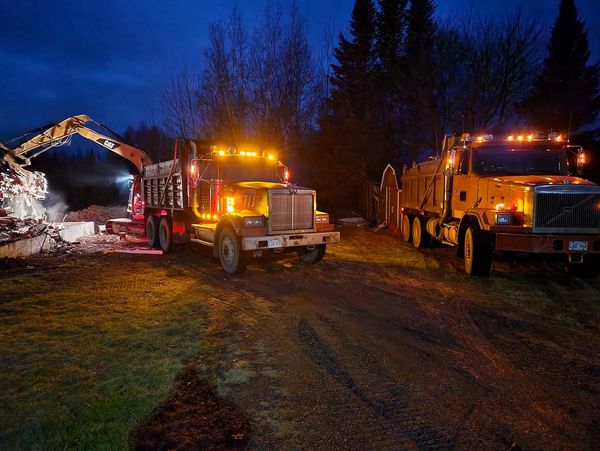 Two illuminated dump trucks and an excavator working at night.