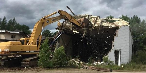 Excavator demolishing a small building on a cloudy day.