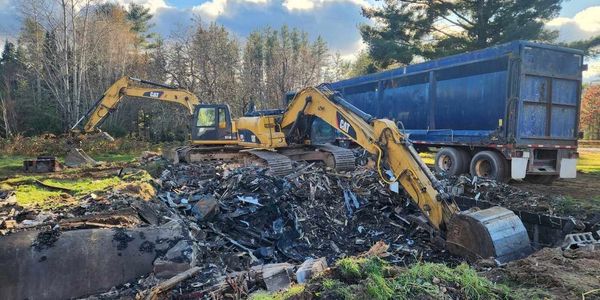Two excavators clearing debris near a large blue dump truck.