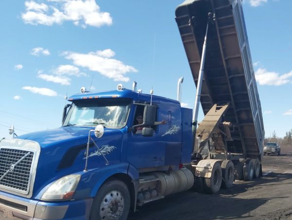 Blue dump truck unloading dirt under a clear sky.
