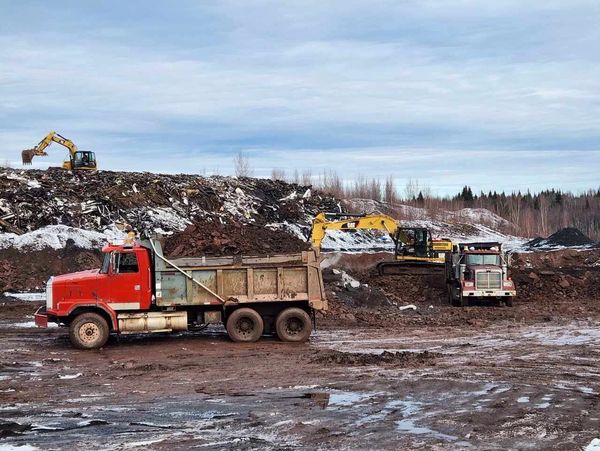 Construction vehicles working on a muddy site with dirt piles and excavators.