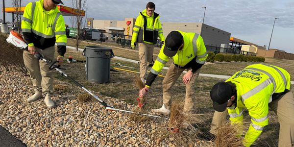 Workers in neon yellow jackets doing landscaping on a rocky ground.