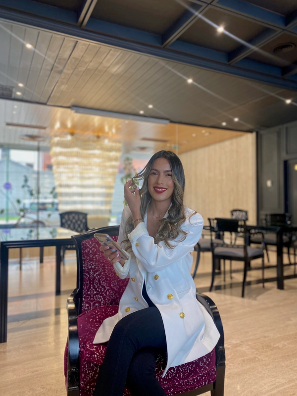 Mujer sonriente con chaqueta blanca sentada en silla roja elegante.