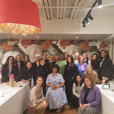 Group photo of diverse women gathered in a decorated room with floral wallpaper.