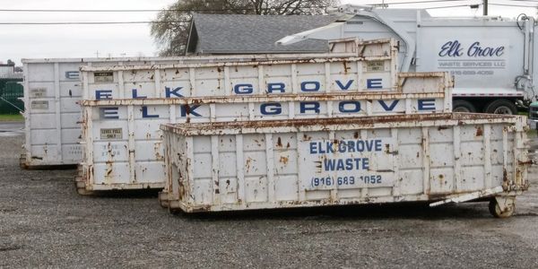 Rusty waste containers and a truck labeled Elk Grove Waste parked outdoors.