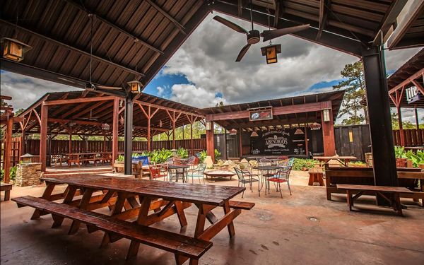 Outdoor seating area with wooden tables and a stage under a cloudy sky.