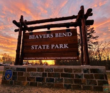 Beavers Bend State Park South Entrance sign with sunset. Road to the Forest Heritage Center.