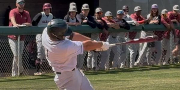Baseball player hitting a ball while others watch.